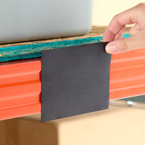 A 4-inch wide magnetic label holder being applied to steel shelving.