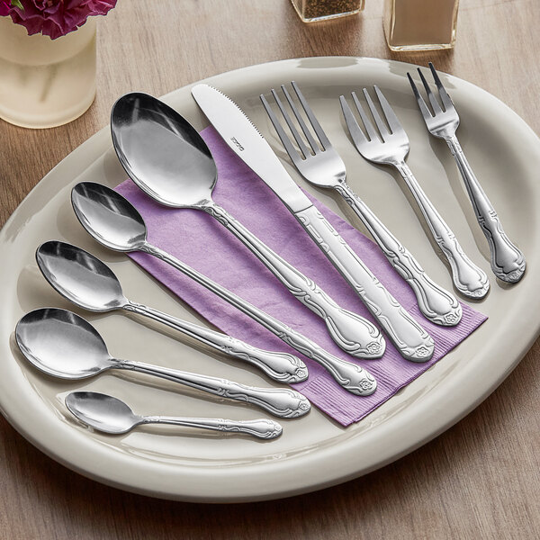A set of stainless steel flatware including spoons, forks, and a knife displayed on a plate with a purple napkin.