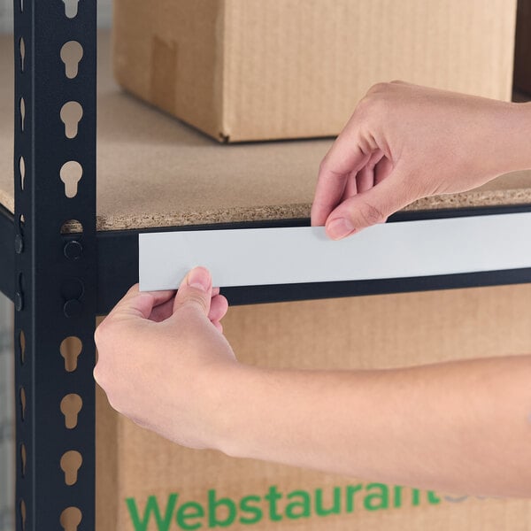 A white slip strip label holder being applied to a metal shelf.