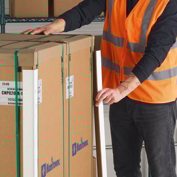 A person in a safety vest is handling a cardboard edge protector next to large packed boxes.