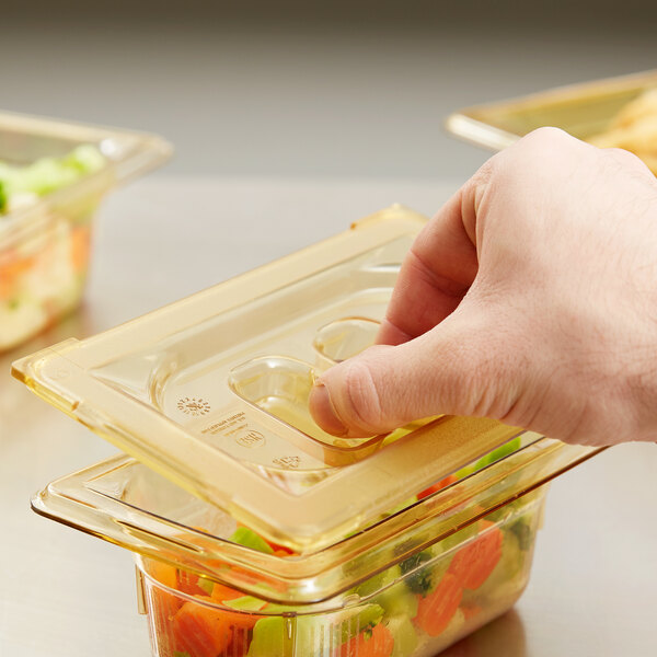 A hand holding a Vollrath Super Pan with amber high heat lid containing food.