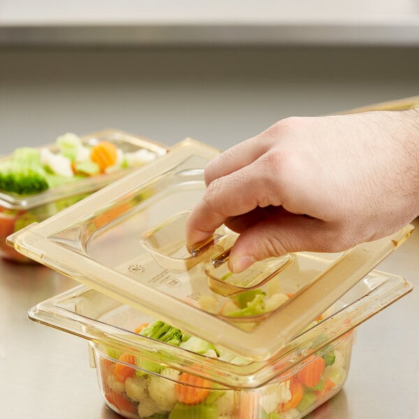 A person's hand pushing a Vollrath Super Pan high heat plastic lid onto a container of food.