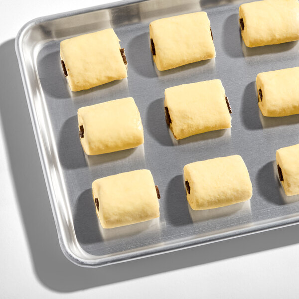 A baking tray with several unbaked small chocolate croissants arranged in rows.