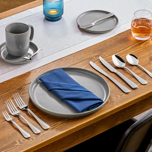 An extra heavy weight stainless steel teaspoon placed on a wooden dining table set with gray dinnerware and silverware.