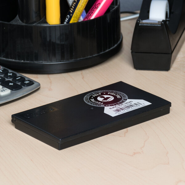 A black pre-inked felt stamp pad on a desk near office supplies.