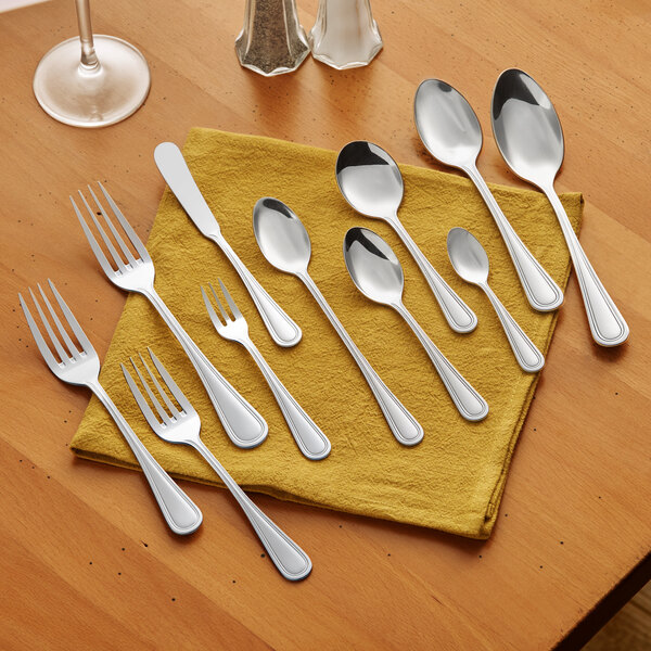 A set of assorted stainless steel flatware including forks, spoons, and a steak knife displayed on a yellow napkin.