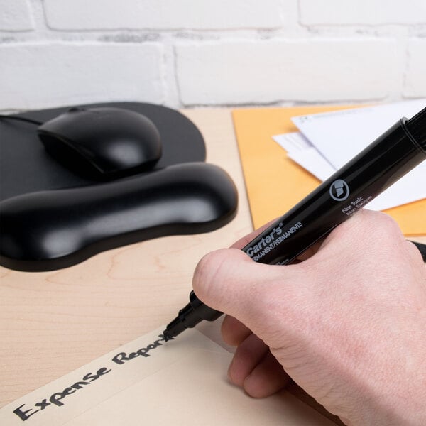 A large black chisel tip permanent marker being used to label a file folder on a desk.