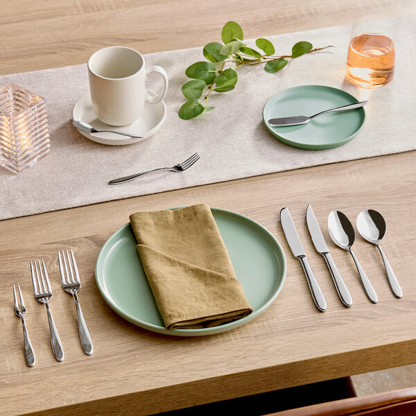 A stainless steel dinner knife placed on a table setting with other cutlery and dinnerware.