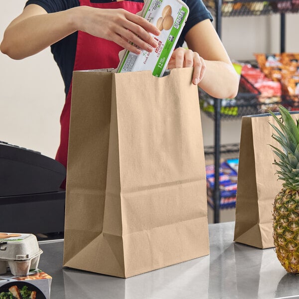 A large brown insulated paper bag being filled with groceries at a checkout counter.