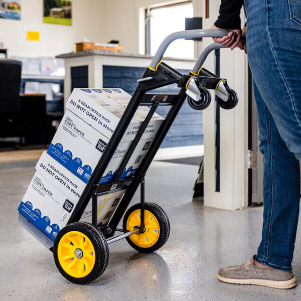 A steel convertible hand truck with yellow wheels being used to transport boxes in an office setting.