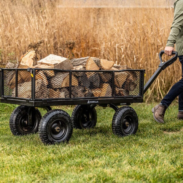A steel utility cart loaded with firewood being pulled across grass.