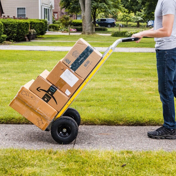 A person using a Gorilla 800 lb. aluminum hand truck to transport several cardboard boxes on a sidewalk.