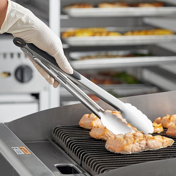 A person in gloves using Tablecraft 2012 12" Ergonomic Locking Tongs to cook food on a grill.