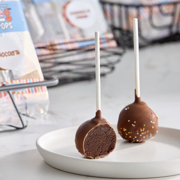 A plate with two chocolate cake pops, one of which is cut in half to show the inside, both covered in chocolate and decorated with colorful sprinkles.