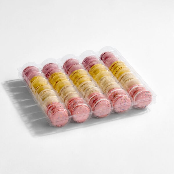 A plastic tray containing an assortment of colorful macarons in pink, yellow, and cream hues.