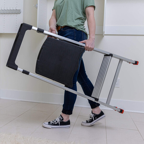 A person carrying a folded aluminum 2-step folding project step stool.