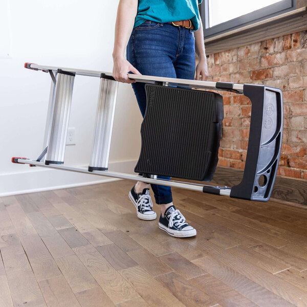A person carrying a Lift Ladders aluminum 3-step folding project step stool indoors.