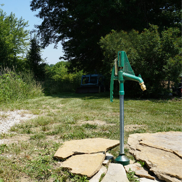 A green non-freeze sanitary ground hydrant with a lever installed outdoors.
