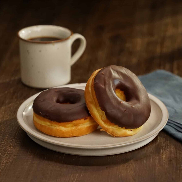 A plate with two chocolate iced donut rings next to a cup of coffee.