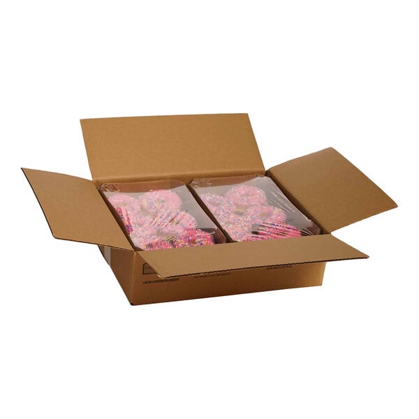 A cardboard box containing two plastic-wrapped trays of pink iced donuts with sprinkles.