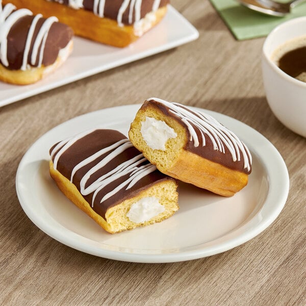 A chocolate iced Long John donut filled with buttercreme and drizzled with white icing, served on a white plate.