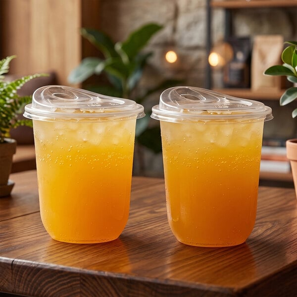 A pair of clear, plant-based plastic sip lids fitted on cold beverage cups filled with iced orange drinks.
