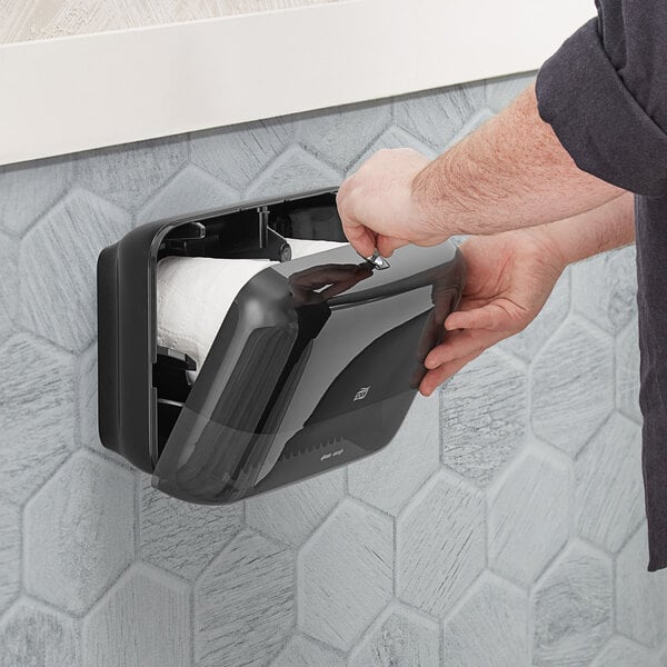 A black wall-mounted double roll toilet tissue dispenser being refilled.