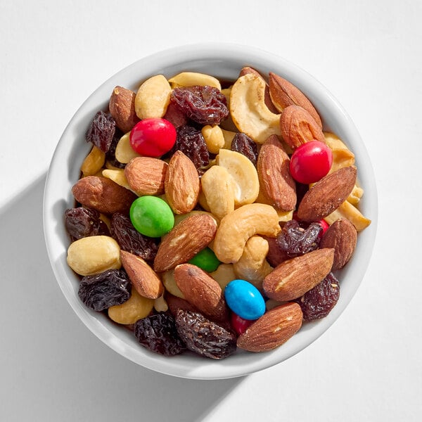 A white bowl filled with a mix of almonds, cashews, peanuts, raisins, and colorful candy-coated chocolates.