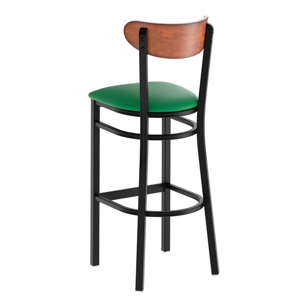A black metal bar stool with a green vinyl seat and an antique walnut wood backrest.