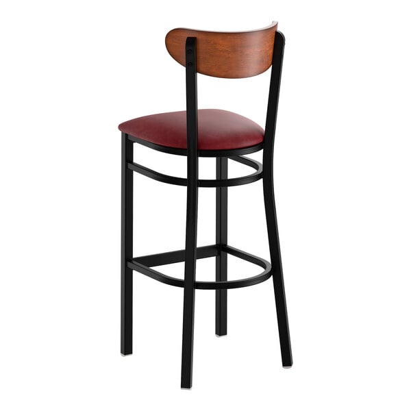A black metal bar stool with a burgundy vinyl seat and an antique walnut wood backrest.