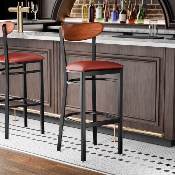 A black metal bar stool with a burgundy vinyl seat and an antique walnut wood backrest.
