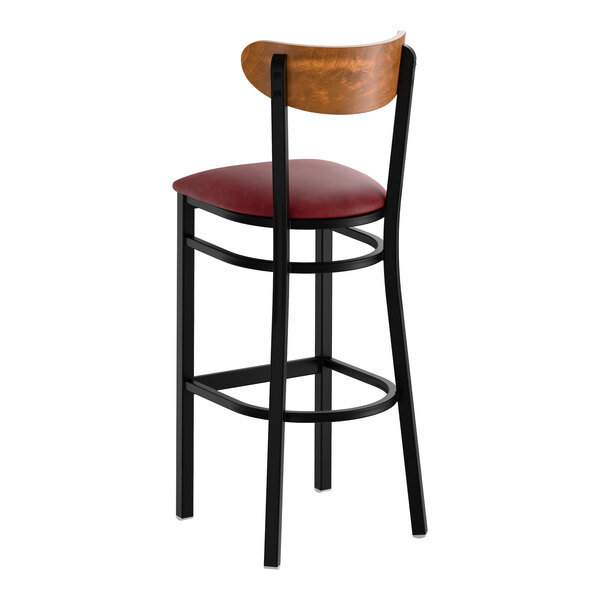 A bar stool with a black metal frame, a burgundy vinyl seat, and a curved wooden backrest.