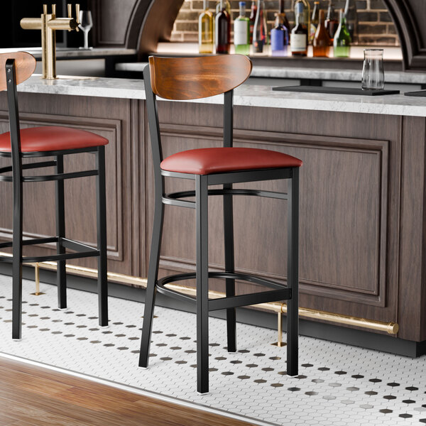 A black metal bar stool with a burgundy vinyl seat and a curved wooden backrest.
