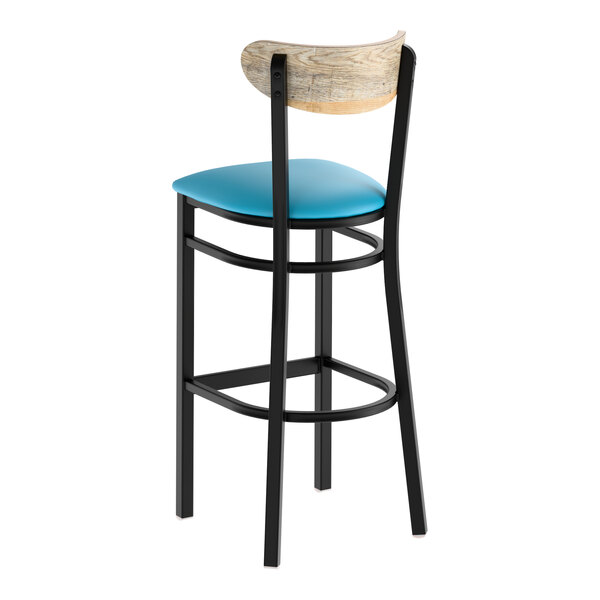 A bar stool with a black metal frame, blue vinyl seat, and a driftwood-finished curved wooden backrest.