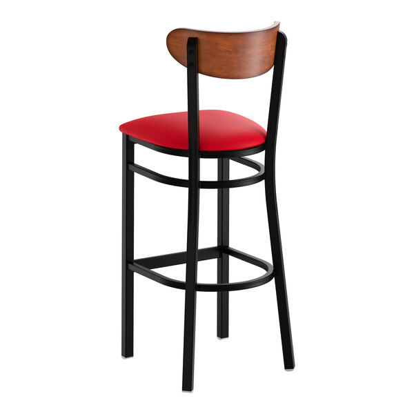 A black metal bar stool with a red vinyl seat and an antique walnut wood backrest.