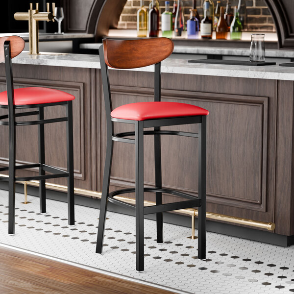 A black bar stool with a red vinyl seat and an antique walnut wood back, shown at a bar counter.