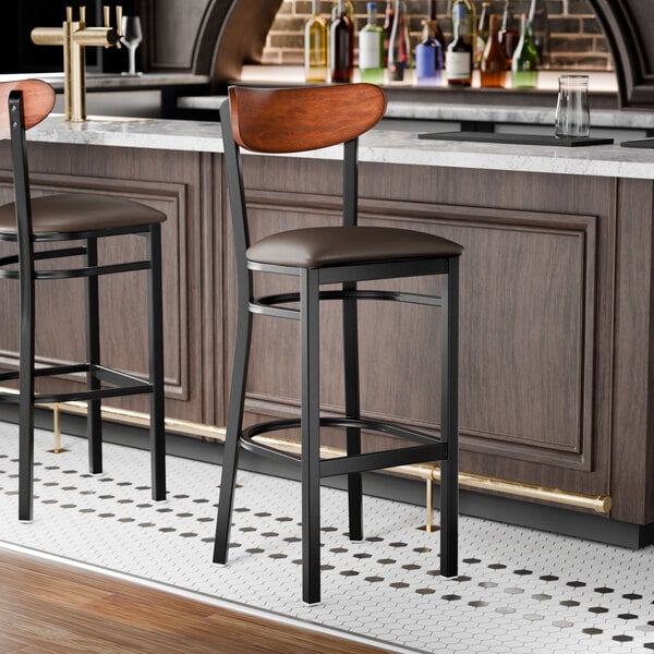 A black finish bar stool with a dark brown vinyl seat and an antique walnut wood back.