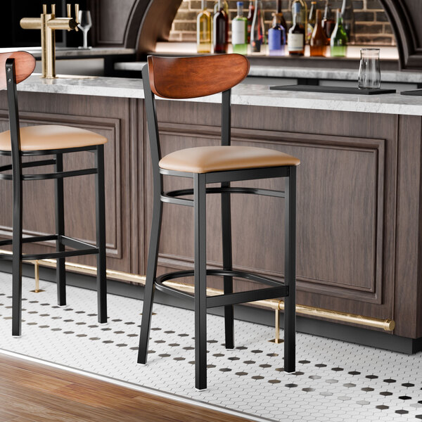 A black metal bar stool with a light brown vinyl seat and an antique walnut wood backrest.