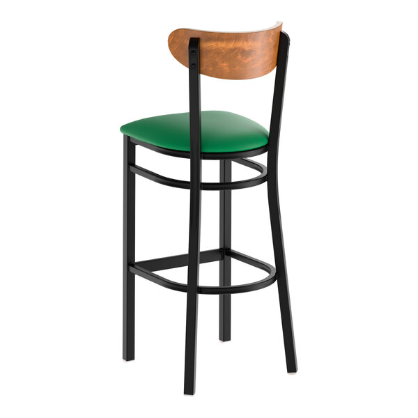 A black metal bar stool with a green vinyl seat and a curved vintage wood backrest.