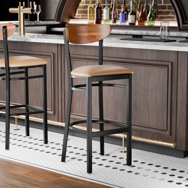 A black metal bar stool with a light brown vinyl seat and a curved vintage wood backrest.
