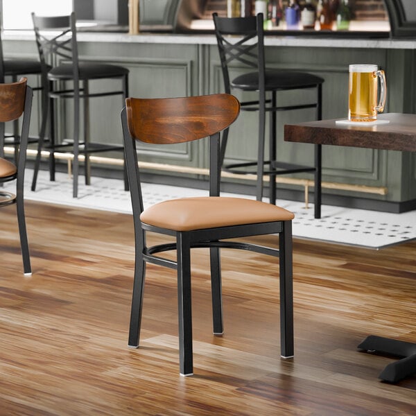 A black metal chair with a light brown vinyl seat and a curved vintage wood backrest.