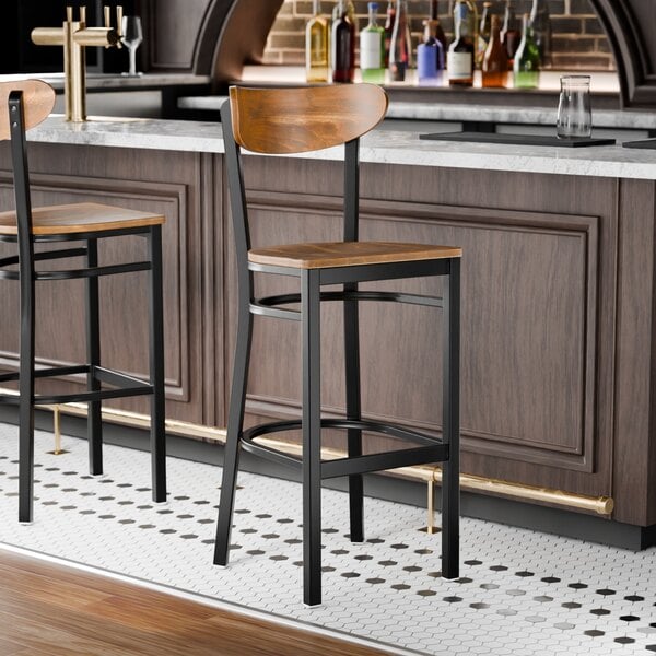 A black metal bar stool with a vintage wood seat and backrest.
