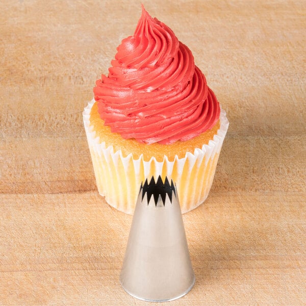 A metal French star piping tip is shown in front of a cupcake with red swirled frosting.