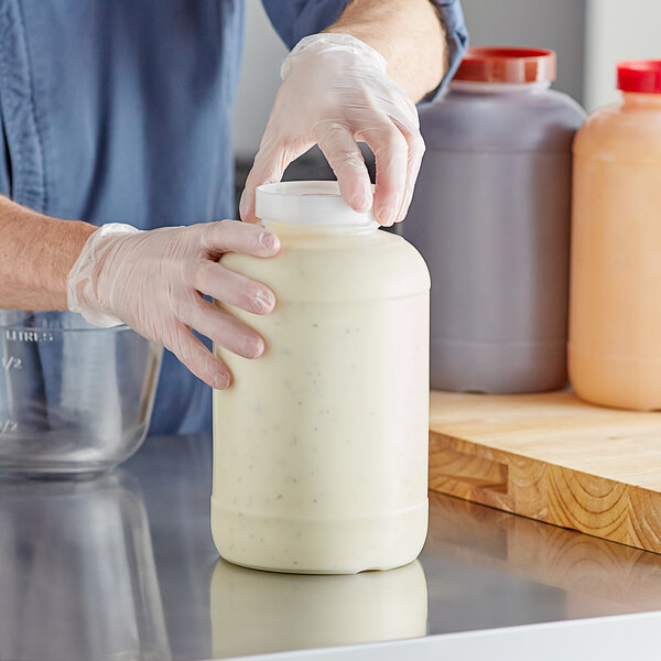 A large one-gallon plastic backup container with a white cap, being handled by a person wearing gloves.
