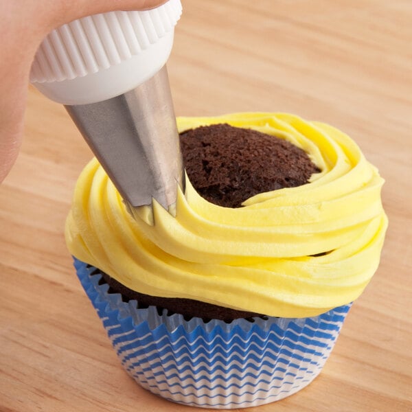 An open star piping tip being used to apply yellow frosting to a chocolate cupcake in a blue and white wrapper.