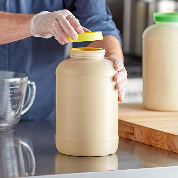 A large beige plastic container with a yellow cap being handled in a kitchen setting.