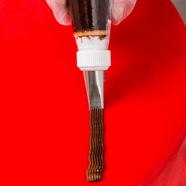 A metal basketweave piping tip being used to pipe chocolate icing onto a red surface.