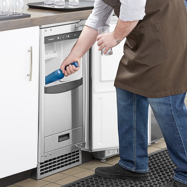 An undercounter Scotsman ice machine with a front-opening door, being used by a person to scoop ice.