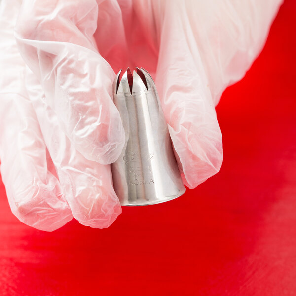 A metal closed star piping tip being held by a gloved hand.