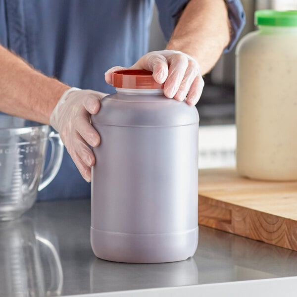A one-gallon plastic backup container with a brown cap being handled by a person wearing gloves.